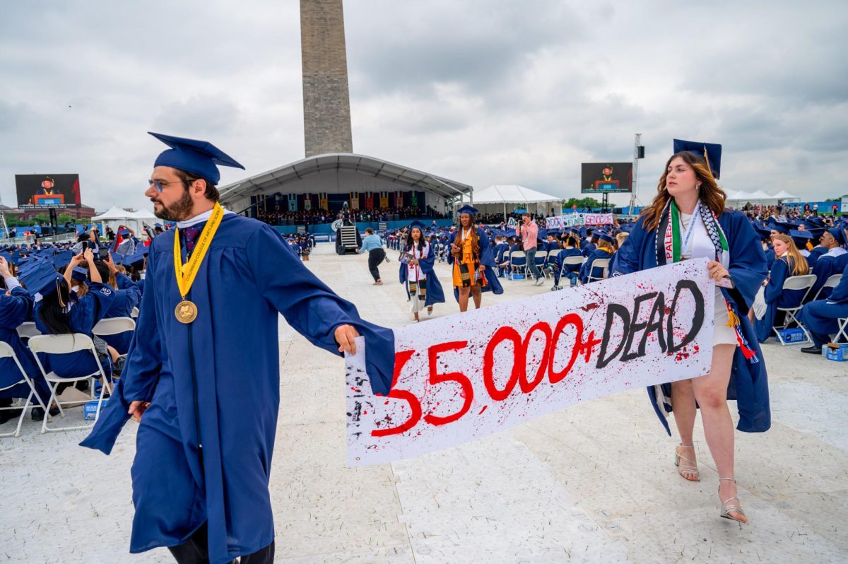 Graduates walk out of the 2024 Commencement Ceremony holding a sign reading "35,000+ Dead."